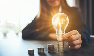 Businesswoman holding and putting lightbulb on coins stack on table for saving energy and money concept